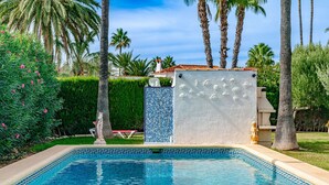 A swimming pool with a decorative tile border, surrounded by palm trees and a hedge.