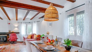 A dining area with a wooden table set for four, surrounded by chairs. A wicker pendant light hangs above the table.