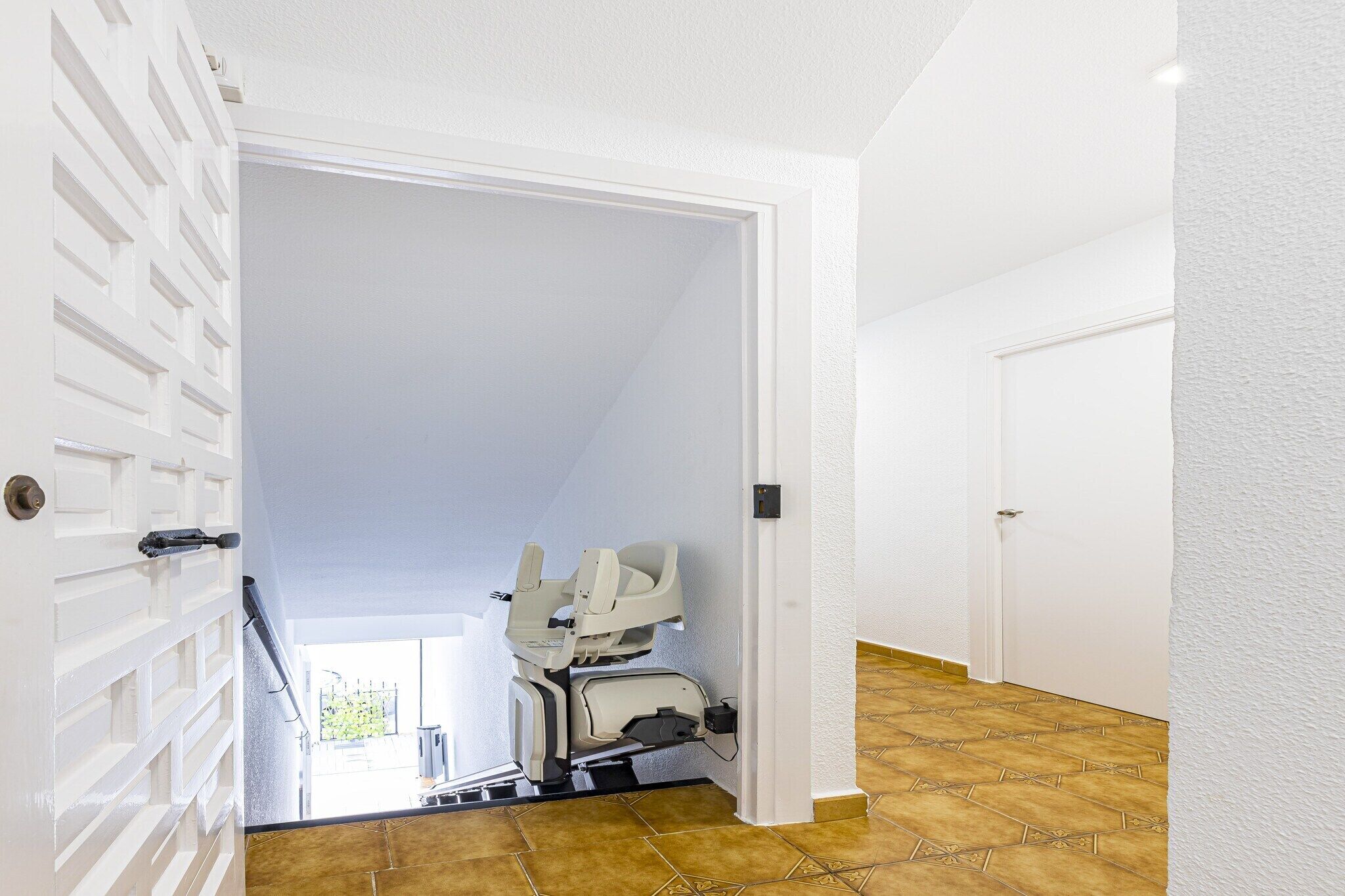 A hallway with a white door, a white wall, and a patterned floor.
