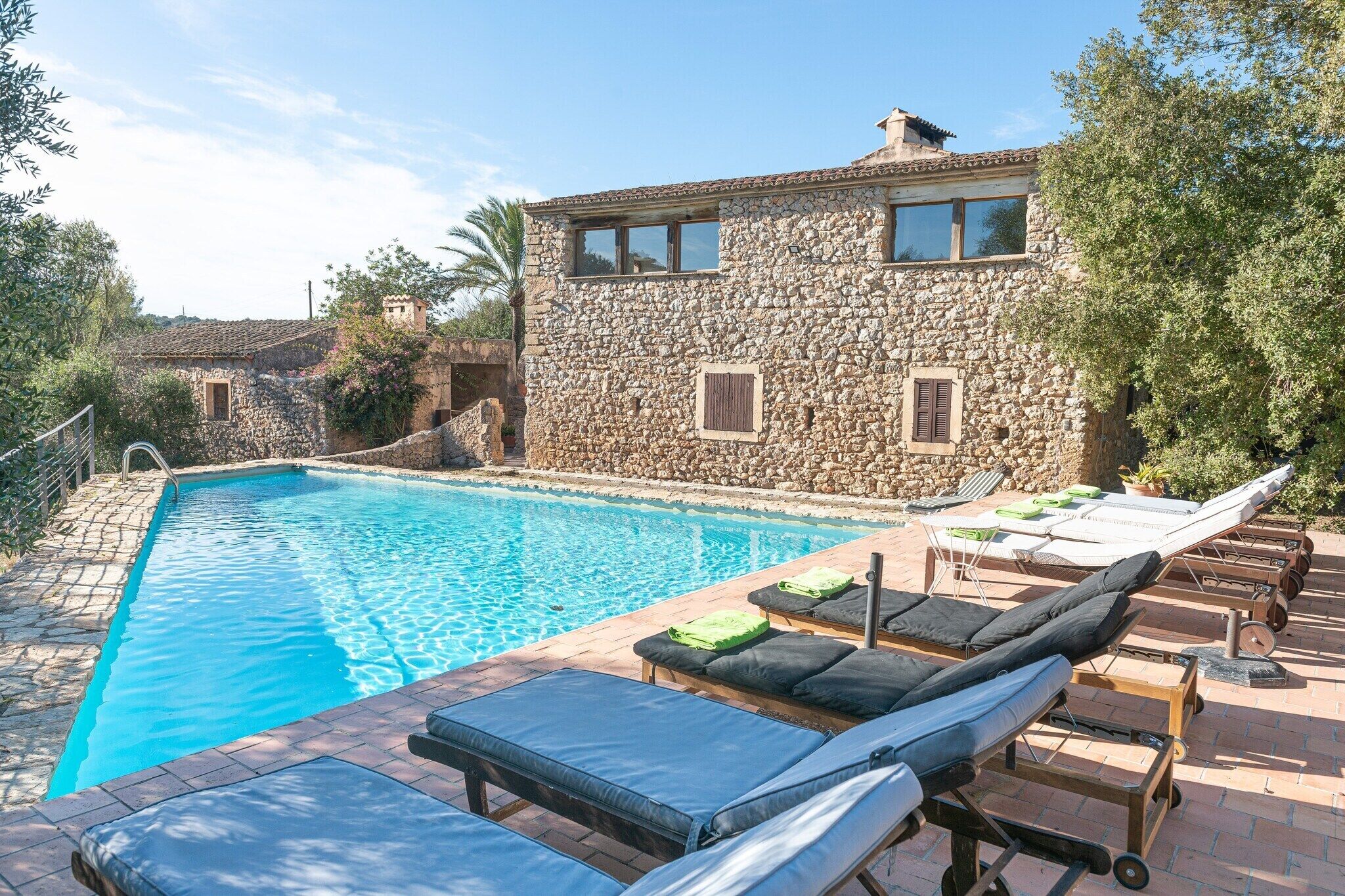 A stone building with a swimming pool and sun loungers.