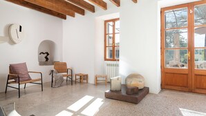 A room with a wooden ceiling, a large wooden door, and a window. There are several chairs and a table. - Son Pastor - Villa With Private Pool In Artà (, Illes Balears)