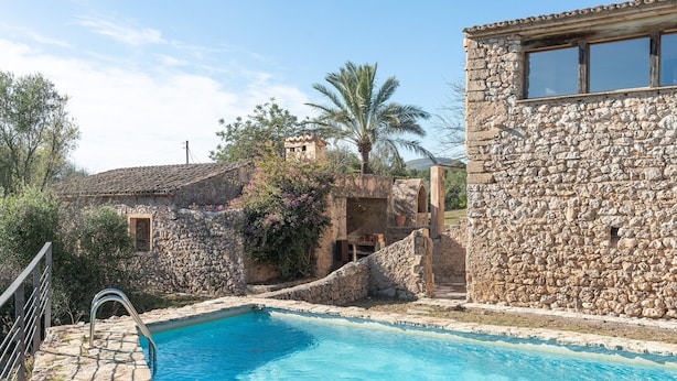 A stone building with a swimming pool, surrounded by trees and a palm tree. - Son Pastor - Villa With Private Pool In Artà (, Illes Balears)