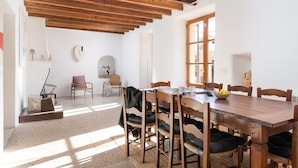 A dining area with a wooden table and chairs, a clock on the wall, and a window providing natural light. - Son Pastor - Villa With Private Pool In Artà (, Illes Balears)