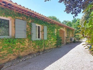 A rustic building with a tiled roof, green shutters, and a gravel driveway.