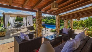 An outdoor patio with wicker furniture, a covered area with a pergola, and a view of a swimming pool.