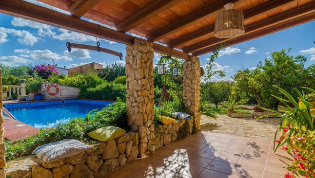 A covered outdoor area with a swimming pool, stone pillars, and a tiled floor.
