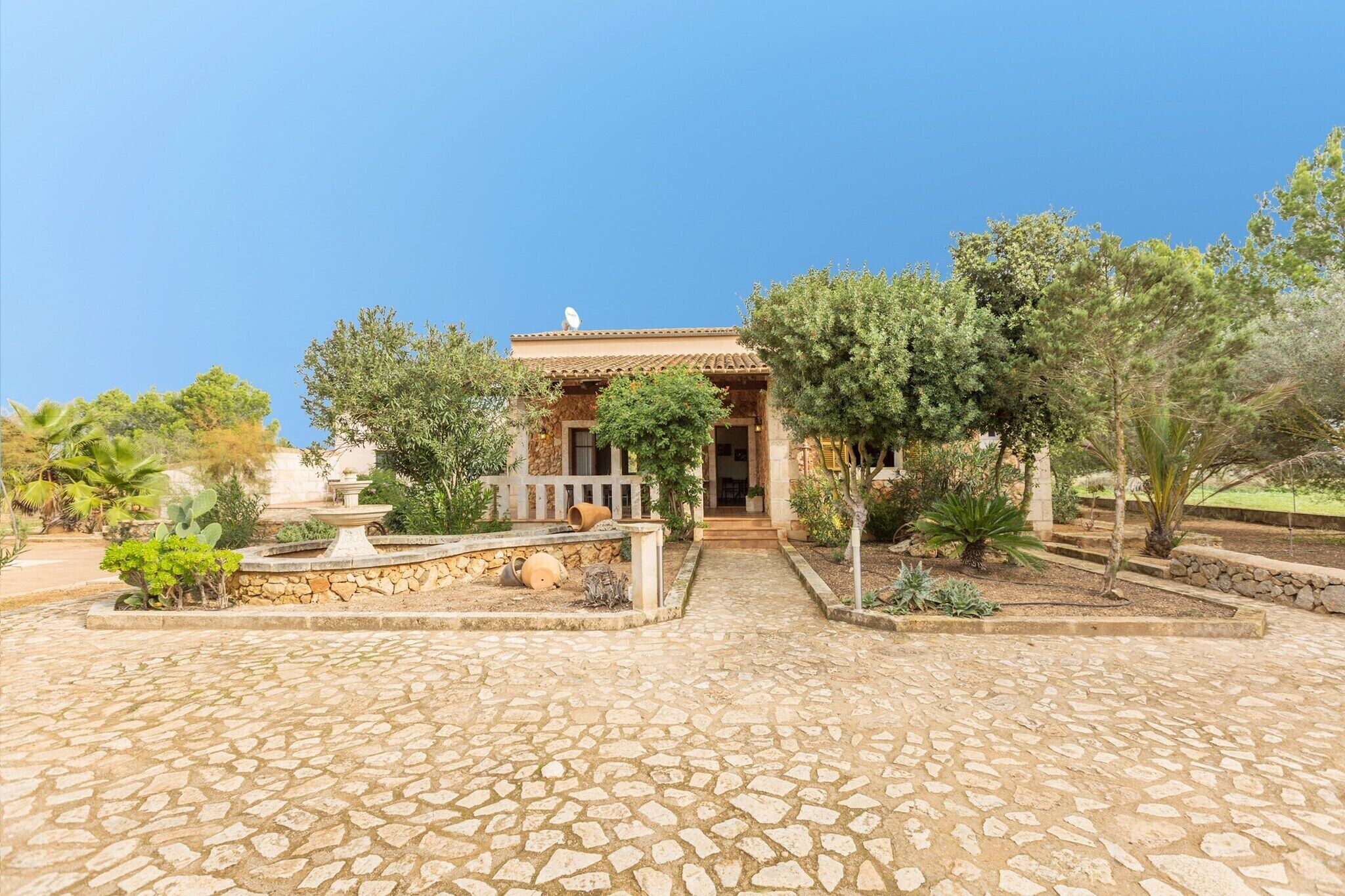 A courtyard with a stone floor, a fountain, and a building with a tiled roof and a satellite dish.