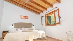 A bedroom with a large bed, wooden ceiling beams, a small bedside table, and a window with shutters.
