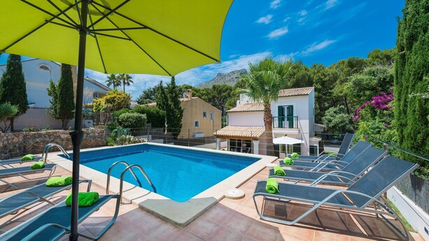 A swimming pool with lounge chairs and a yellow umbrella, surrounded by greenery and buildings. - El Pinar - Villa With Private Pool. Free Wifi (Cala Sant Vicenç, Illes Balears)