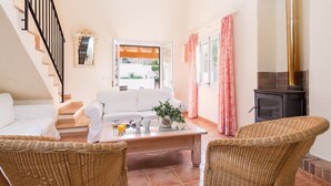 A cozy living room with a white sofa, a coffee table, wicker chairs, a fireplace, and a staircase leading to another level. - El Pinar - Villa With Private Pool. Free Wifi (Cala Sant Vicenç, Illes Balears)