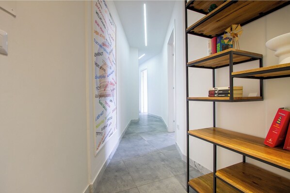 Un couloir avec un nuage de mots fixé au mur, une bibliothèque en bois et un sol carrelé.