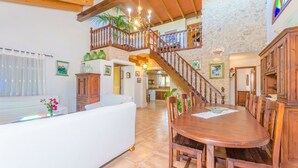 A spacious living area with a high ceiling, wooden staircase, and a dining table set for four. - Can Reure (can Paris) - Villa With Private Pool (Inca, Illes Balears)