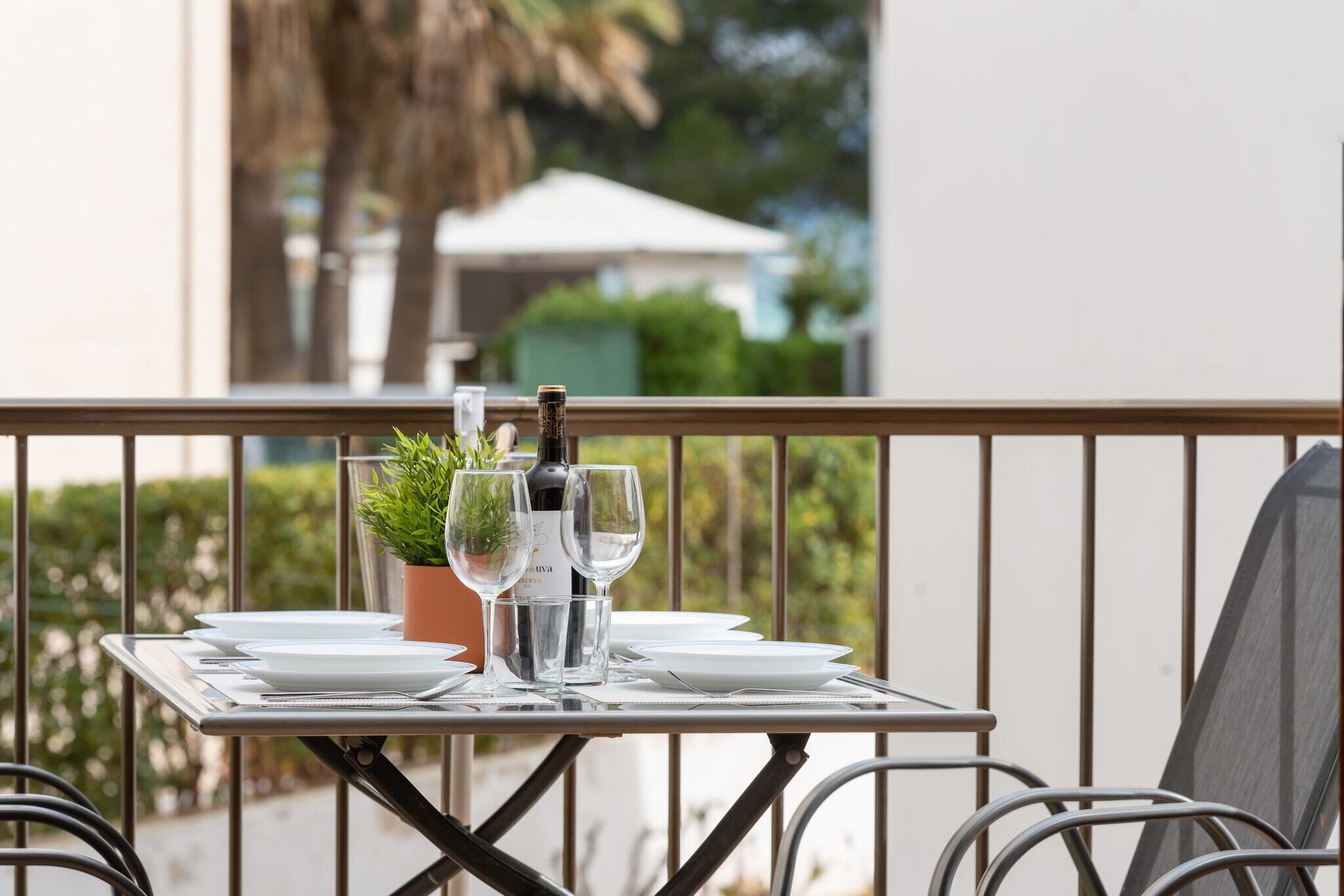 Un tavolo apparecchiato su un balcone con vista su vegetazione e un edificio sullo sfondo.
