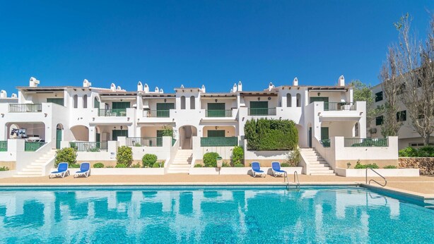 A hotel with a swimming pool, multiple balconies, and a clear blue sky.