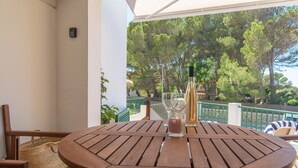A wooden table with a bottle and glasses on a balcony with a view of trees.