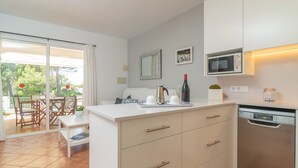 A modern kitchen with a white countertop, a built-in microwave, and a dishwasher. There is a dining area with a table and chairs visible through a sliding glass door.