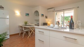 A compact kitchen with a dining area, white cabinets, a refrigerator, a dining table with chairs, and a window with a view of greenery.