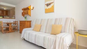 Un salon comprenant un canapé, une table à manger avec des chaises, un coin cuisine et une étagère fixée au mur.