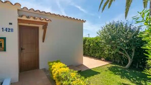 Un bâtiment avec une porte portant l’inscription « 142B » et un petit jardin agrémenté de fleurs jaunes et d’un palmier.
