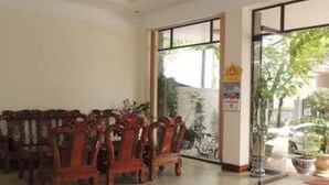 A lobby with wooden chairs arranged in rows, a glass door leading outside, and a potted plant near the entrance.