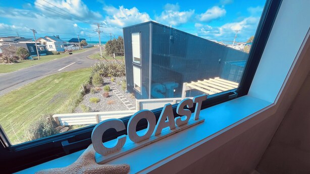 A window with a view of a coastal area, a starfish decoration, and the word "COAST" on the window sill. - “ VITAMIN SEA “ 
Beach ~ House  (Riverton / Aparima)