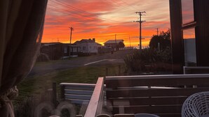 A view from a window with the word "COAST" on the sill, overlooking a sunset with buildings and power lines in the distance. - “ VITAMIN SEA “ 
Beach ~ House  (Riverton / Aparima)