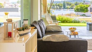 Een moderne woonkamer met een bank, stoelen en uitzicht op een tuin en een waterpartij.