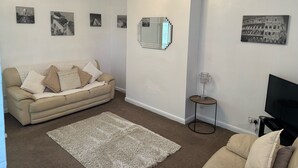 A living room with a beige sofa, a white rug, and a flat-screen TV. - Home and Away (Eaglescliffe)