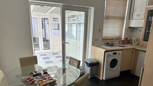 A compact kitchen with a washing machine, a small sink, and a glass dining table with chairs. - Home and Away (Eaglescliffe)