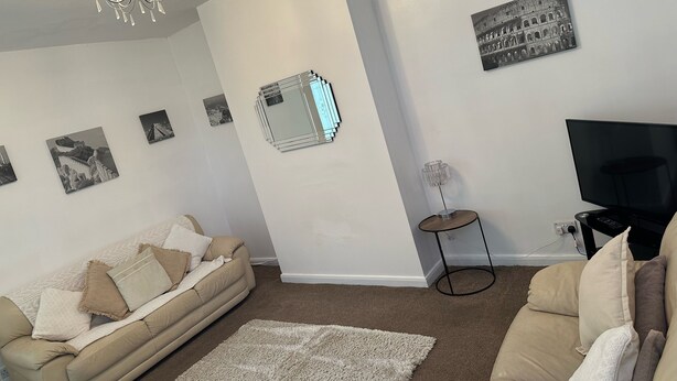 A living room with a beige sofa, a white rug, a chandelier, a mirror, and a framed picture of the Colosseum. - Home and Away (Eaglescliffe)