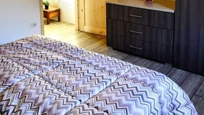 Une chambre avec un plafond en bois, un lit recouvert d’une couverture à motifs, une commode et un tableau accroché au mur.