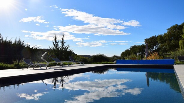 Un ciel bleu azur parsemé de nuages, une piscine et des chaises longues.