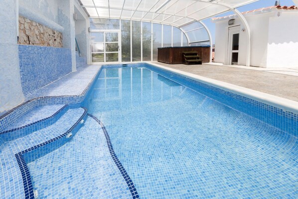 Une piscine intérieure à l’eau d’un bleu limpide, avec des marches carrelées et un espace abrité comprenant un jacuzzi.