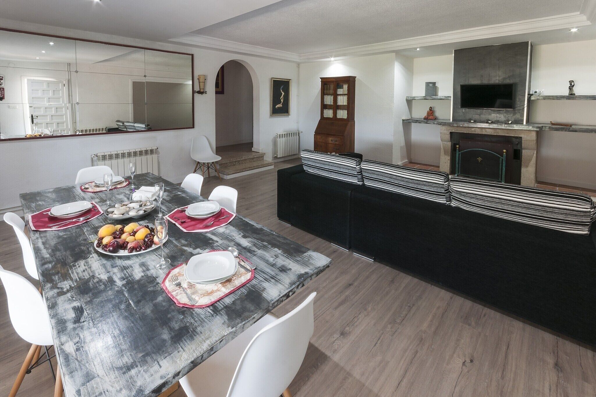 Un coin repas avec une grande table dressée pour quatre personnes, un canapé noir et une cheminée.