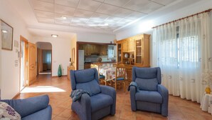 A spacious living room with two blue armchairs, a dining area with a table and chairs, and a kitchen in the background. - Portilet - Villa With Private Pool In Barx (Barx, Valencia)