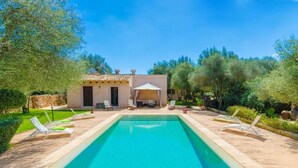 Una piscina rectangular con sillones de descanso y un área de estar techada en un jardín ajardinado.