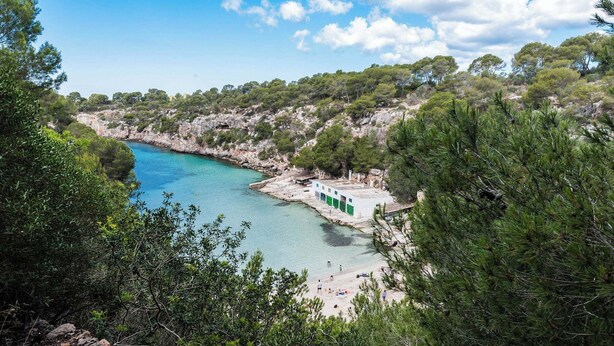 Zona costera con playa, acantilados rocosos y un pequeño edificio con puertas verdes.