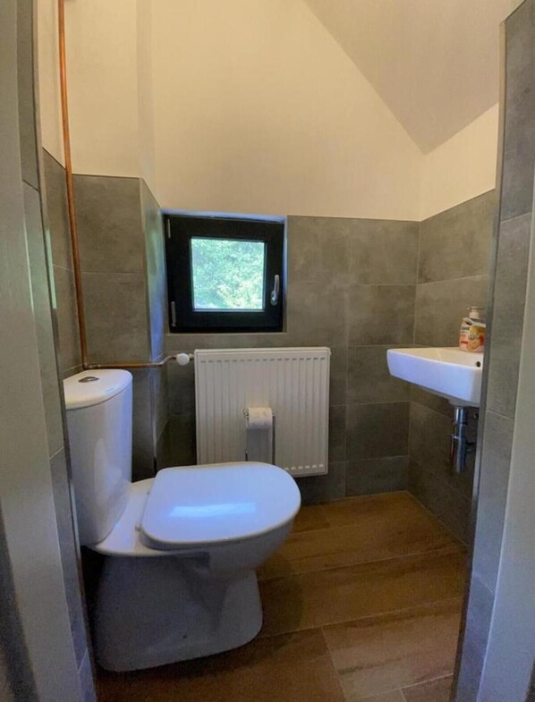 Un baño compacto con inodoro, una pequeña ventana, un radiador y un lavabo.