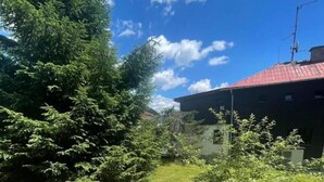 Un césped verde con un edificio de techo rojo, árboles y un cielo azul despejado.