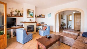 Ein Wohnzimmer mit Fernseher, Sofa, Sessel, Couchtisch, Kamin und Regalen mit Dekoration.