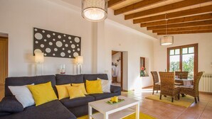 A modern living room with a grey sofa, yellow cushions, a white coffee table, and a dining area with wicker chairs. - Shostalet - Villa With Private Pool In Algaida (Algaida, Illes Balears)