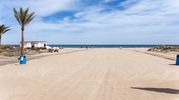 Ein Sandstrand mit einem kleinen weißen Gebäude, Palmen und einem klaren Himmel.
