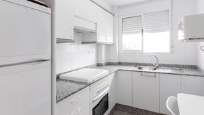 Eine kleine Küche mit weißen Schränken, einem eingebauten Backofen, einer Arbeitsplatte aus Granit und einem Fenster mit Jalousien.