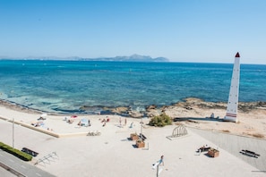 A beach with a tall white lighthouse, clear blue water, and rocky shoreline.