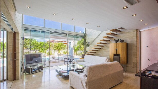 Ein modernes Wohnzimmer mit Glastür zum Balkon, einer Couch, einem Couchtisch und einem Fernseher.
