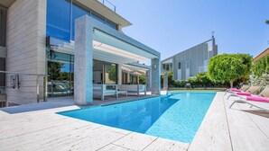 Ein moderner Poolbereich mit klarem, blauem Pool, Liegestühlen und einem zeitgemäßen Gebäude mit großen Fenstern.