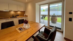 A modern kitchen with wooden cabinets, a dining table with chairs, and a view of a green landscape through a sliding glass door. - Apartment in Saalfelden Near Ski Slopes (Saalfelden am Steinernen Meer)