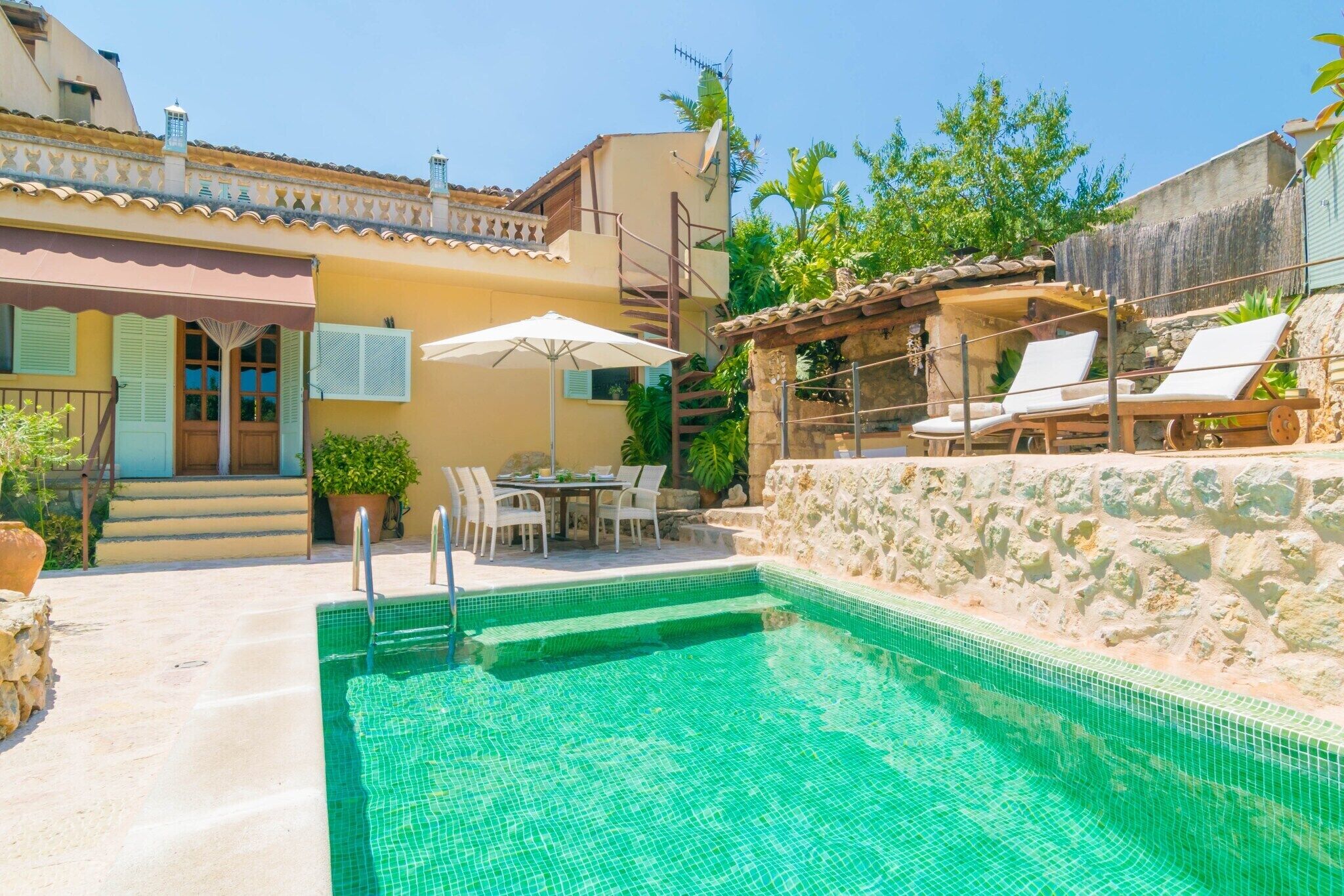 A swimming pool with a stone wall, outdoor seating, and a staircase leading to a second floor.