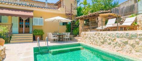 A swimming pool with a stone wall, outdoor seating, and a staircase leading to a second floor.