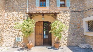 A stone building with a wooden door, two potted plants, and a tiled roof.